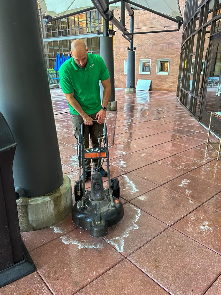 Technician machine-scrubbing an exterior tiled walkway