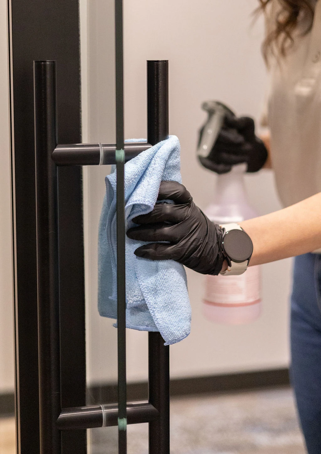 Close-up of a gloved technician wiping a glass door handle with a microfiber cloth