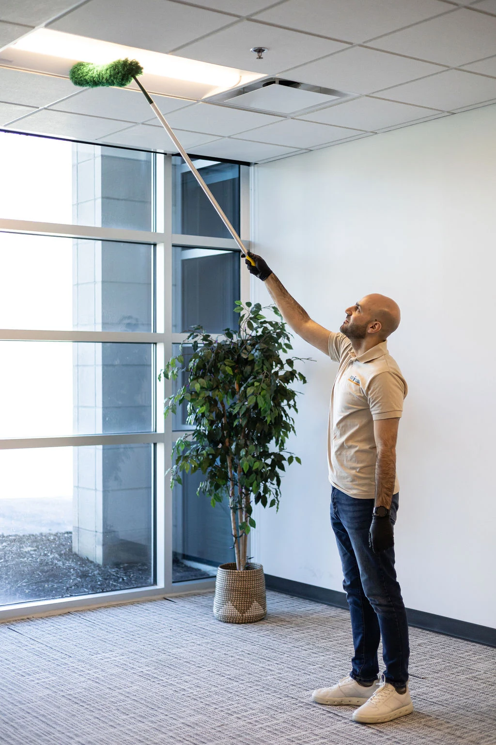 Technician high-dusting an office ceiling vent with an extension duster