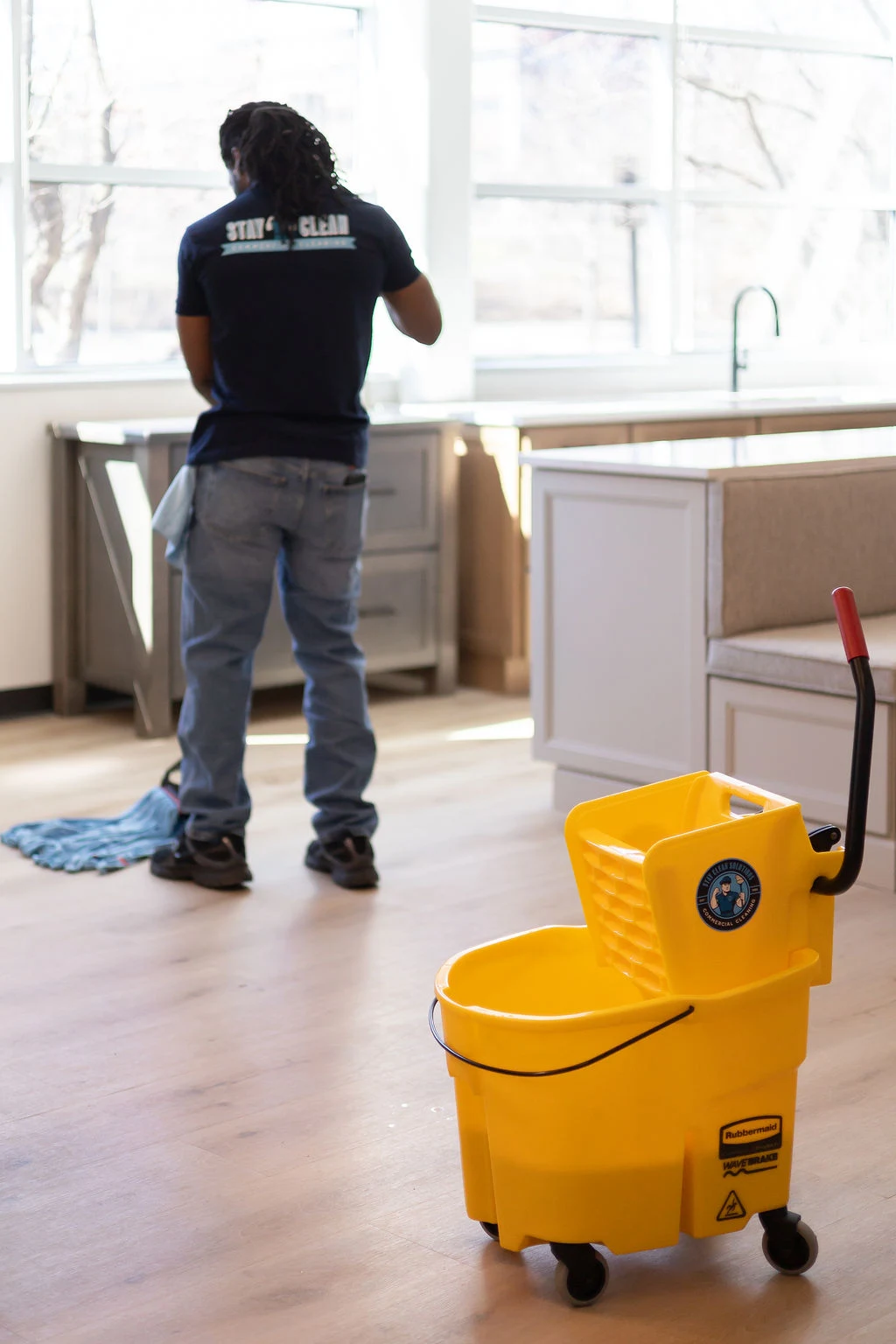 A cleaner working alone in an empty commercial break area with an unattended mop bucket