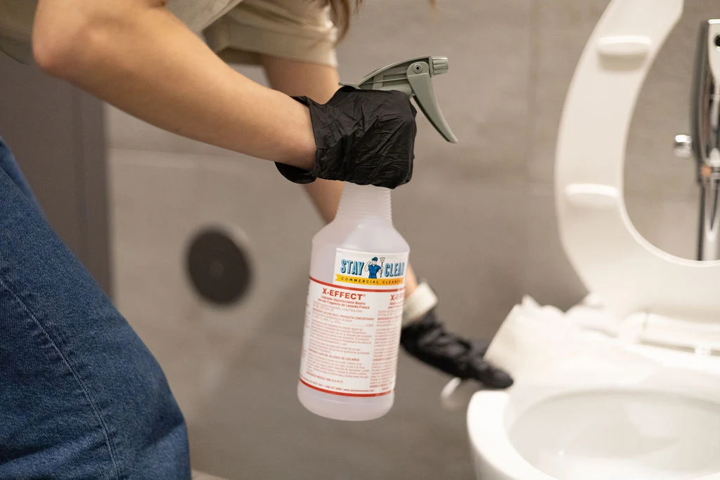 Gloved technician applying disinfectant in a commercial restroom